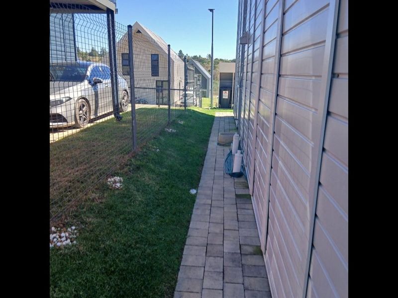 A side exterior view of the property featuring a paved walkway, siding cladding, and wire mesh fencing along the boundary.