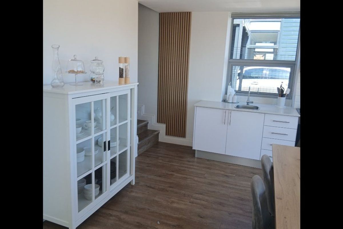 A modern kitchen area featuring white cabinetry, a stainless steel sink, wood-look laminate flooring, and decorative slatted wall paneling.