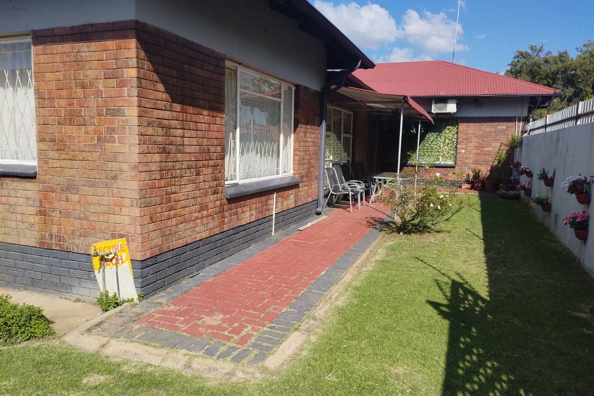 Rear exterior view of the house featuring a brick facade, a paved walkway, and a well-maintained lawn area.