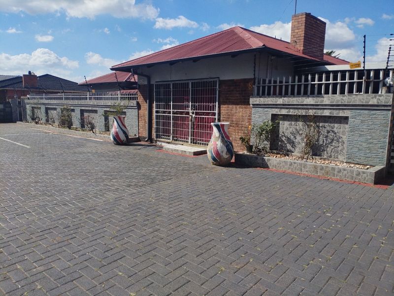Front exterior view of a house featuring a paved driveway, brick facade, stone cladding accents, and secure metal gate entrance.
