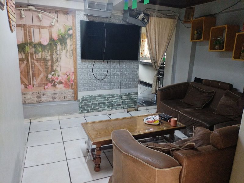 A living room area featuring tiled flooring, wall-mounted television, and built-in shelving, requiring cosmetic updates to improve the overall aesthetic and finish.