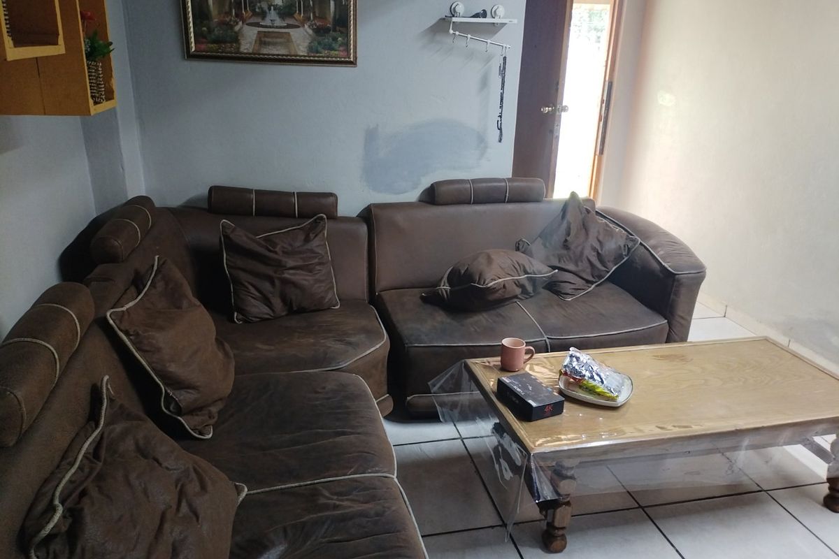 A living room area featuring tiled flooring and access to an adjacent space, showing signs of wear on the walls.