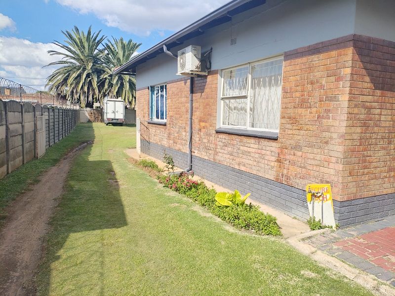 Rear exterior view of the house featuring a brick facade, security window bars, an external air conditioning unit, and a fenced garden area.
