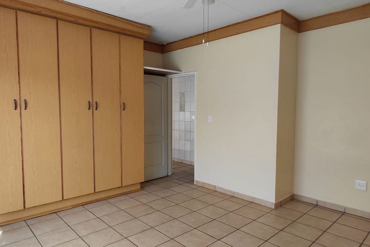 A spacious, empty bedroom featuring neutral tiled flooring, extensive built-in wooden cupboards, and classic timber crown molding.