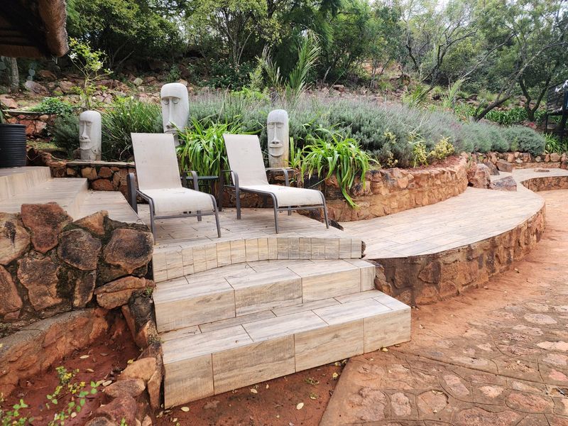 A well-maintained outdoor patio area featuring stone retaining walls, tiled steps, and landscaped garden surroundings.