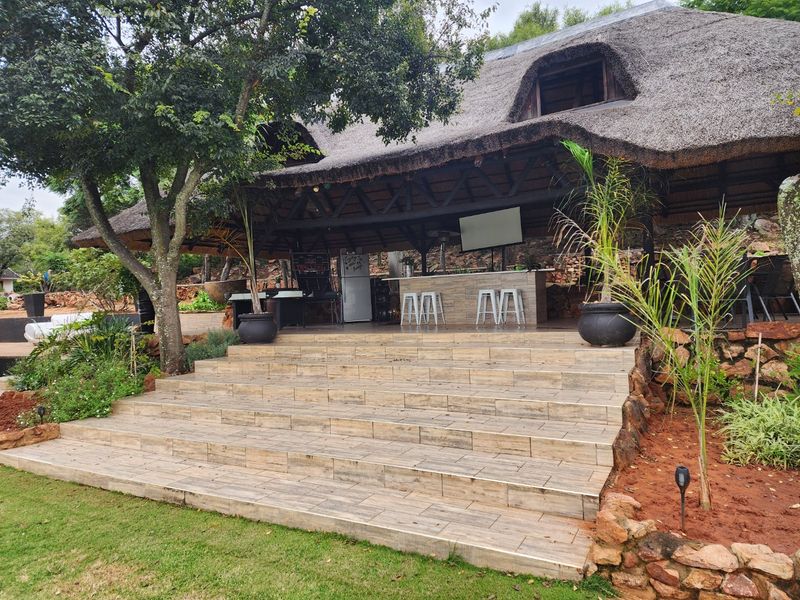 A spacious outdoor entertainment area featuring a thatched roof, exposed timber trusses, and a built-in bar, accessible via wide tiled stairs.