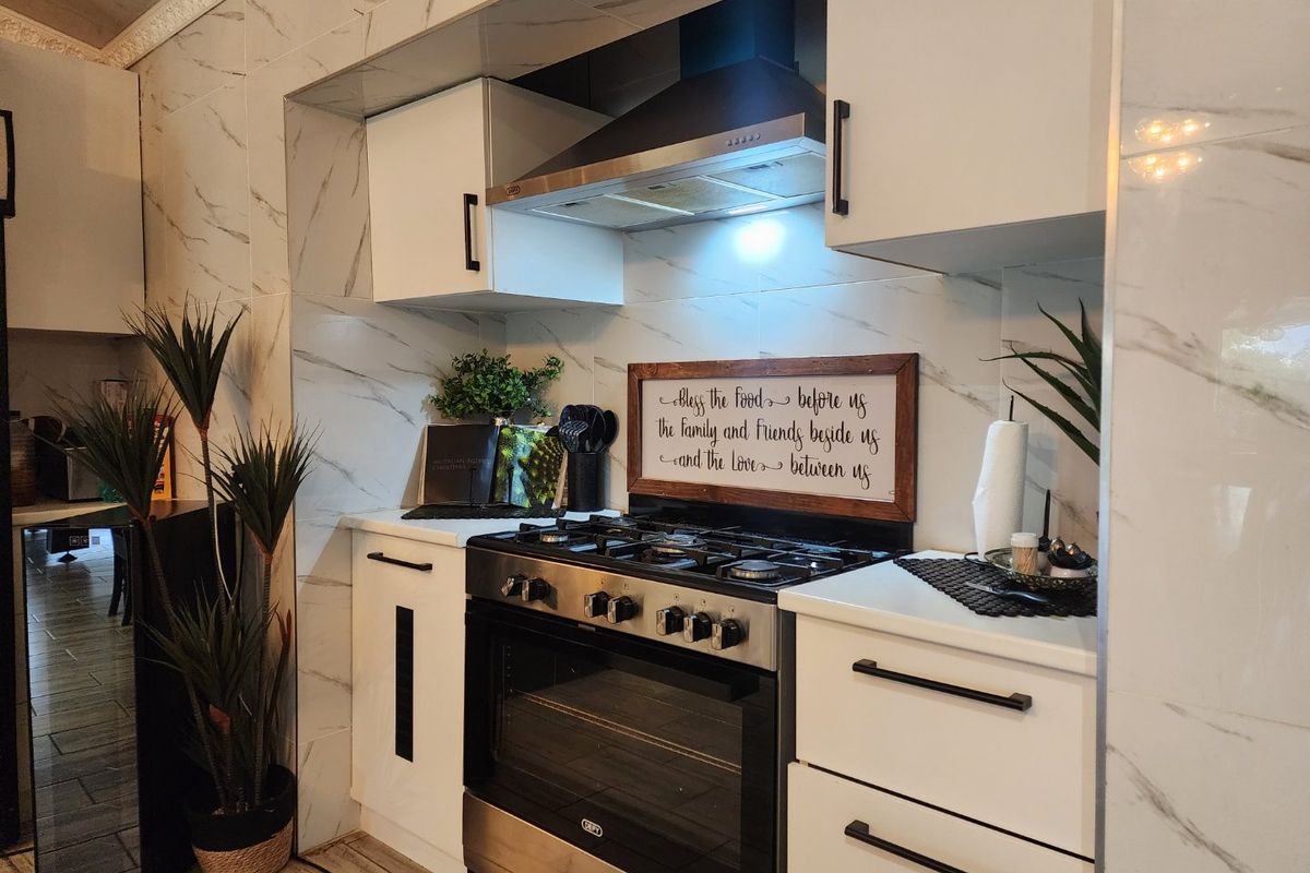 Modern kitchen featuring white cabinetry, marble-look wall tiling, and a stainless steel gas stove with an integrated extractor fan.