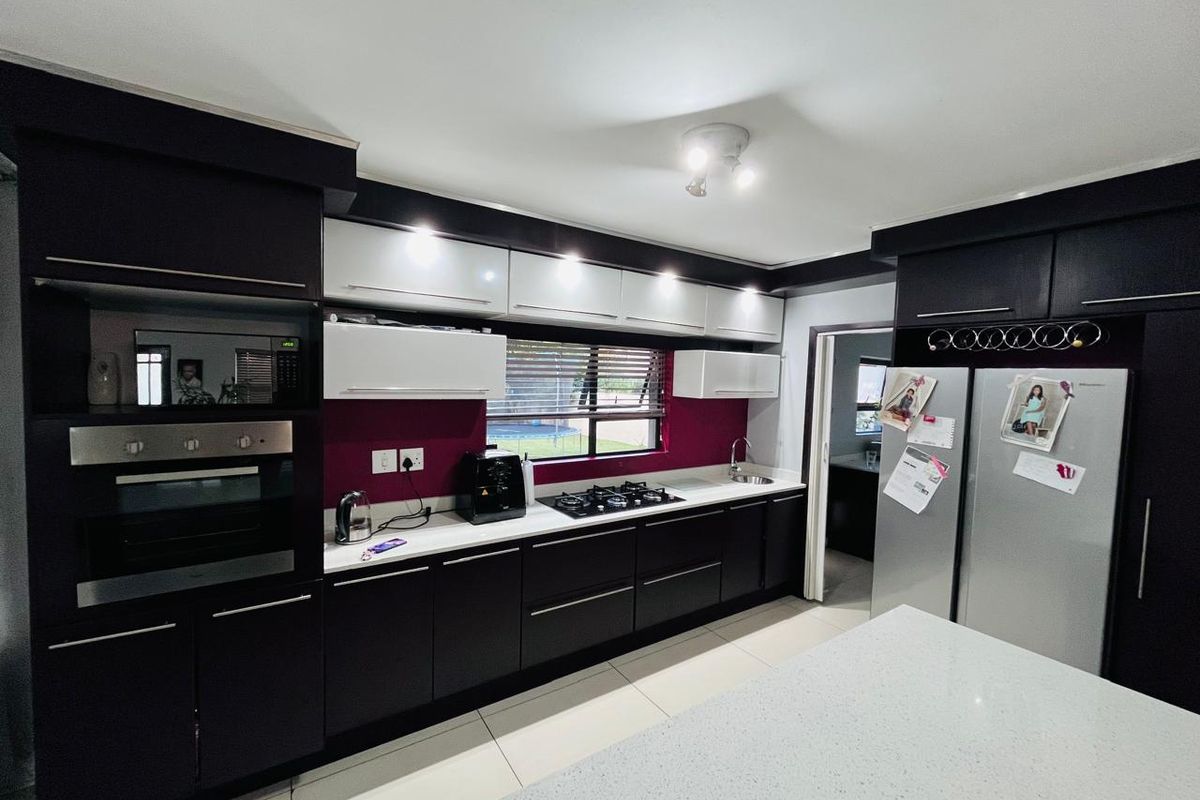 Modern kitchen featuring dark cabinetry, contrasting white upper cabinets, stone countertops, built-in oven, gas hob, and a sleek tiled floor.