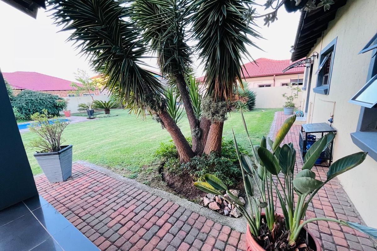 A well-maintained rear garden featuring a paved patio area, established landscaping, and a swimming pool in the background.