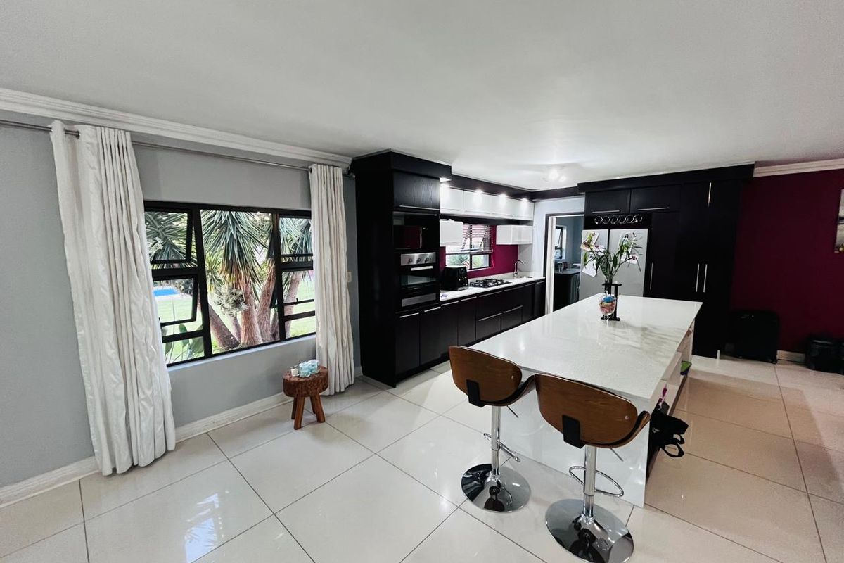 Modern kitchen featuring a large central island with stone countertops, dark cabinetry, built-in appliances, and polished tiled flooring.