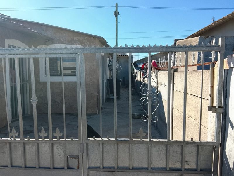Front view of the property featuring a metal security gate, precast concrete boundary wall with security spikes, and a paved entrance area.