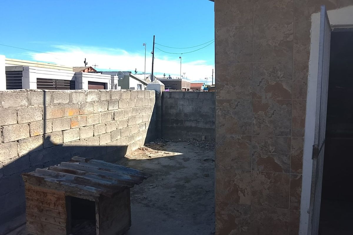 A small, enclosed rear yard area featuring concrete block boundary walls and tiled exterior wall cladding, currently with an unpaved ground surface.