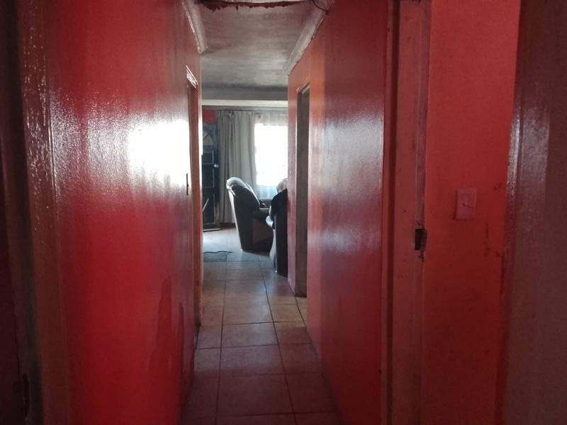 A narrow interior hallway featuring tiled flooring and bright red painted walls, leading towards an adjacent living area.