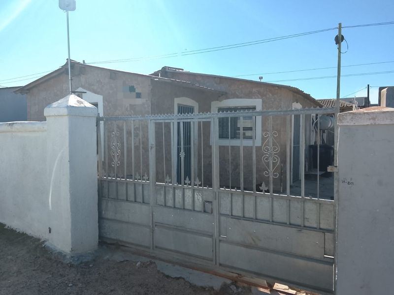 Front elevation of a house featuring a metal security gate and perimeter wall, showing signs of weathered exterior finishes.