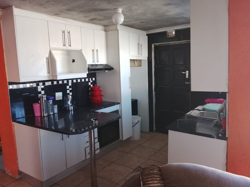 A functional kitchen featuring white cabinetry, black stone countertops, and tiled flooring, requiring some cosmetic updates to the ceiling and finishes.