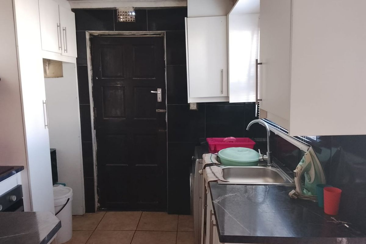 A compact kitchen featuring white cabinetry, dark tiled splashbacks, and a stainless steel sink, requiring some cosmetic updates to improve its overall condition.