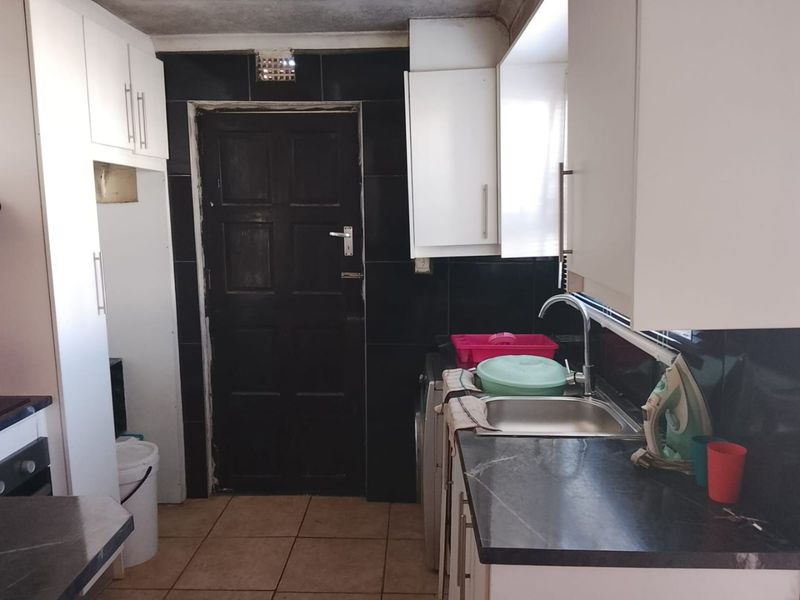 A compact kitchen featuring white cabinetry, dark tiled splashbacks, and a stainless steel sink, requiring some cosmetic updates to improve its overall condition.