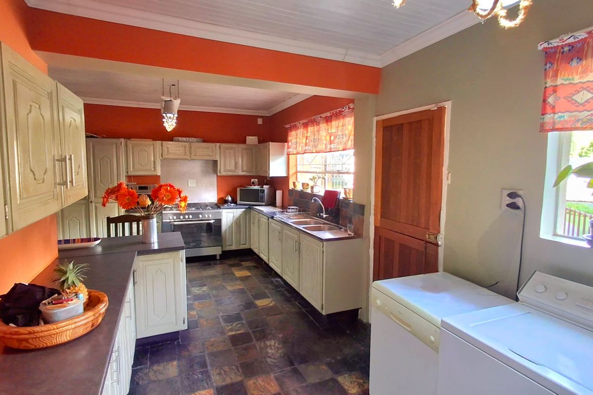 A functional kitchen featuring built-in cabinetry, a stainless steel sink, and a freestanding oven, finished with slate tile flooring and a timber door.