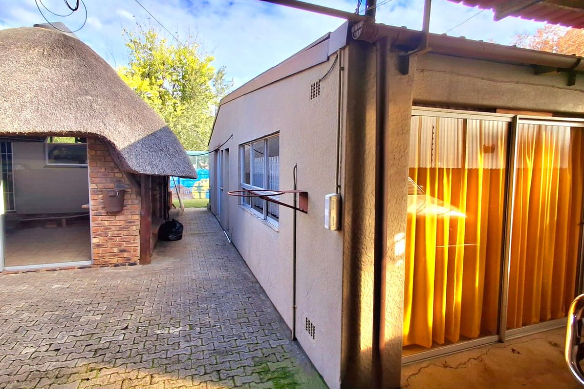 Rear exterior view showing a paved walkway between a thatched structure and a secondary building with sliding glass doors.