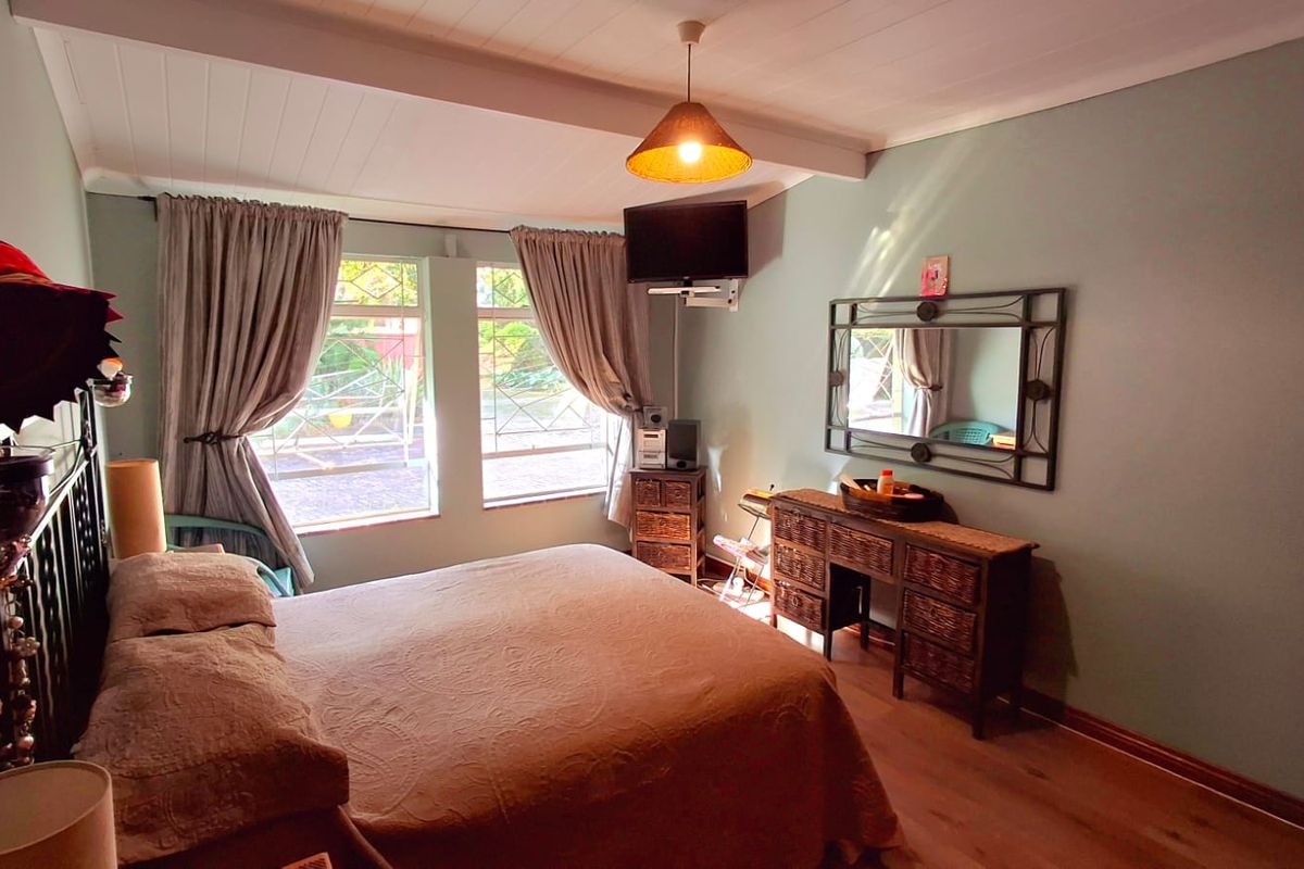A comfortable bedroom featuring timber-look flooring, a timber-paneled ceiling, and windows fitted with security bars.