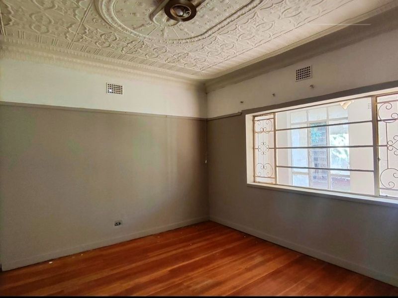 An empty bedroom featuring original pressed metal ceilings, hardwood flooring, and security bars on the window, offering a classic architectural foundation.