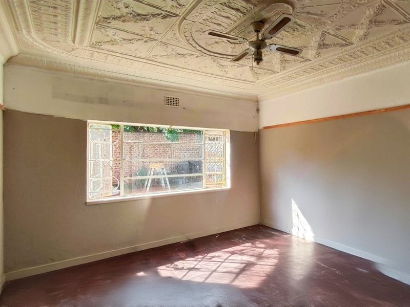 Empty living room featuring a classic ornate pressed metal ceiling, ceiling fan, and large steel-framed window with security gate.