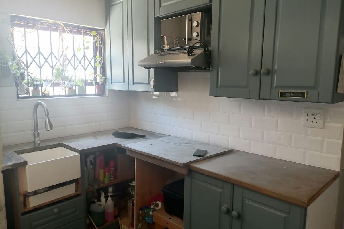 A compact kitchen featuring dark grey cabinetry, a white farmhouse sink, subway tile backsplash, and a built-in extractor fan with microwave housing.