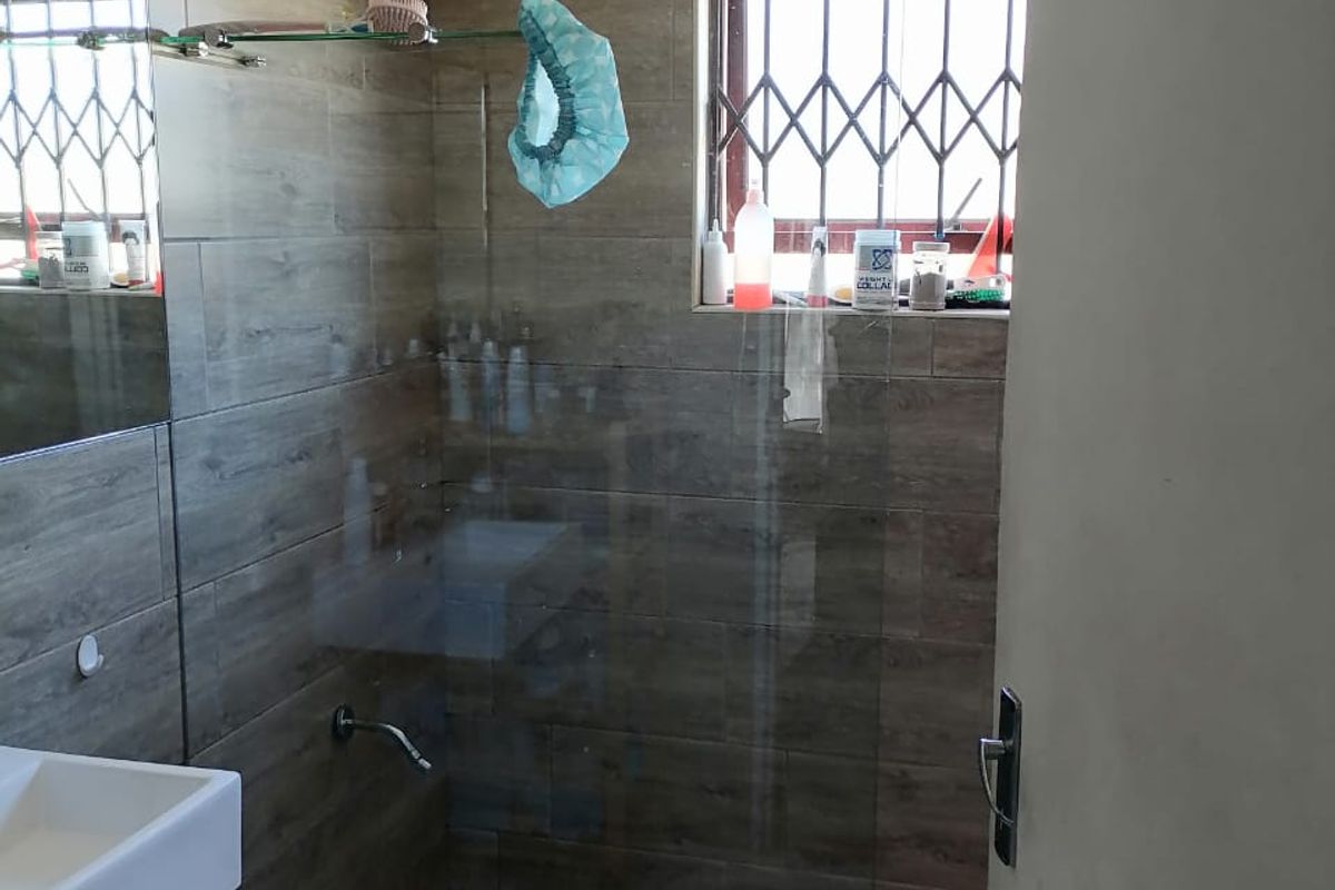 Modern bathroom featuring a walk-in shower with wood-look wall tiles, mosaic floor tiling, a glass shower screen, and a wall-mounted basin.