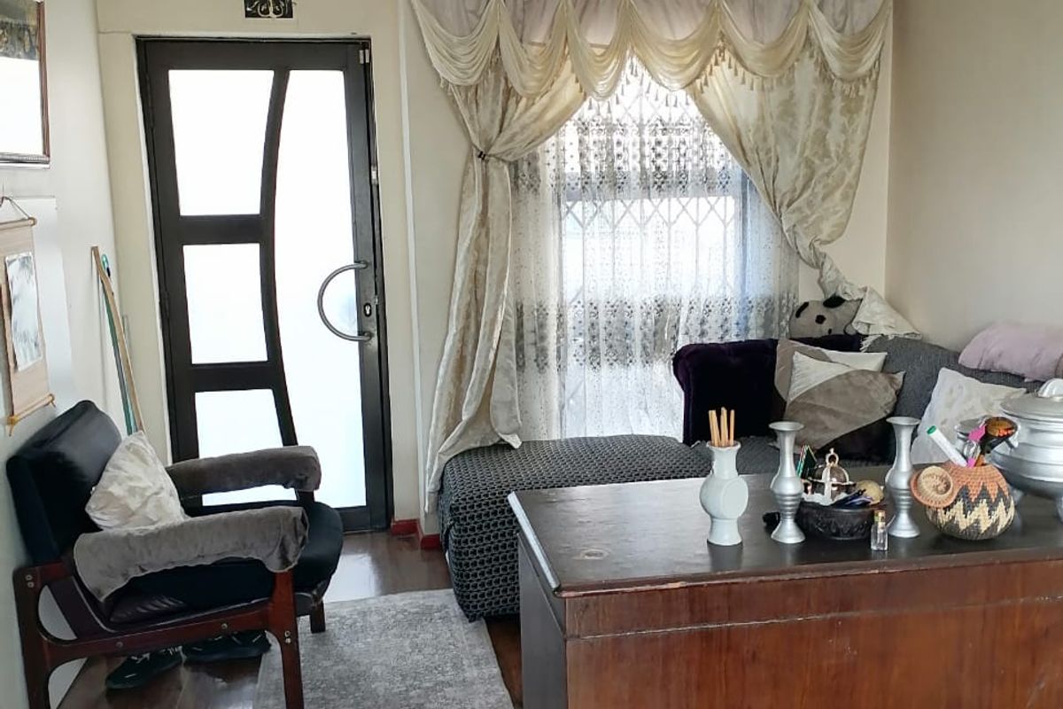 A living room area featuring laminate flooring, a modern glass-panelled entrance door, and a window with decorative curtains.