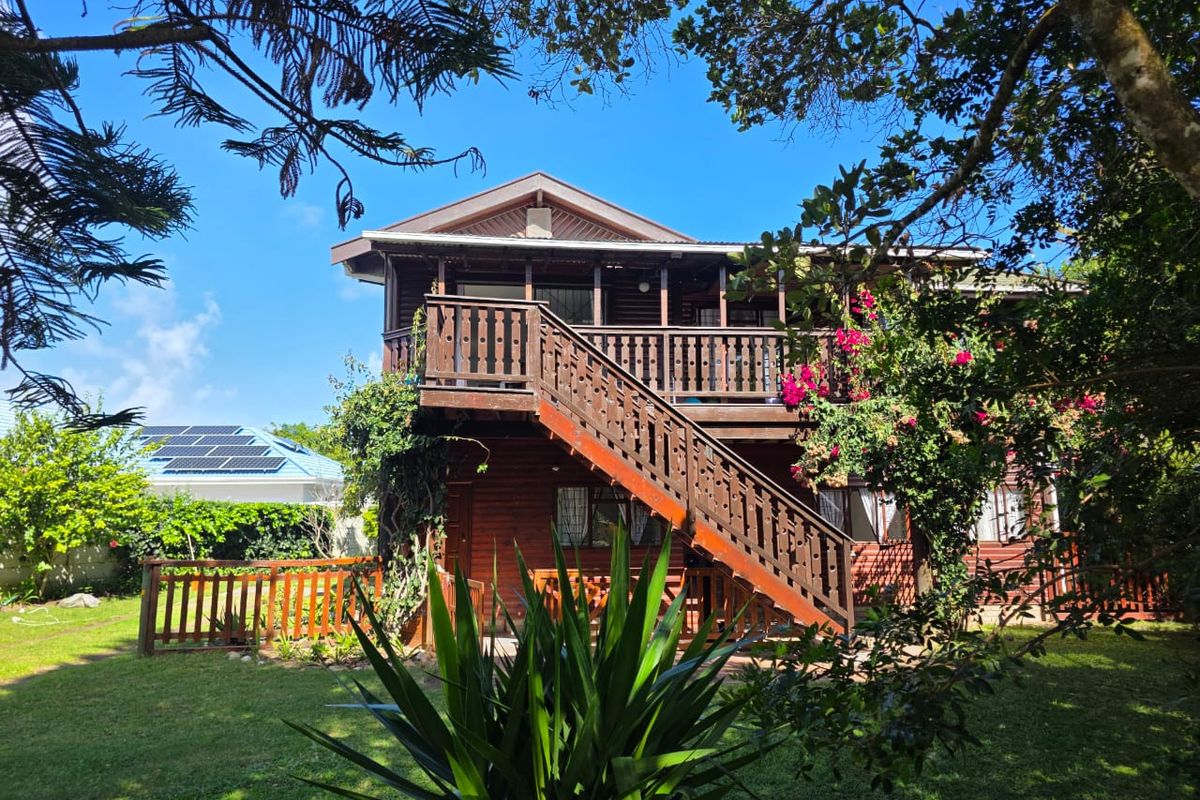 Rear view of a two-story timber-clad house featuring an external staircase leading to an upper-level balcony, set within a landscaped garden.
