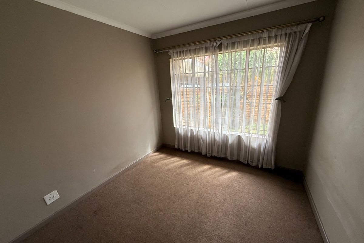 A vacant bedroom featuring neutral wall tones, carpeted flooring, and a large window with installed curtain rods.