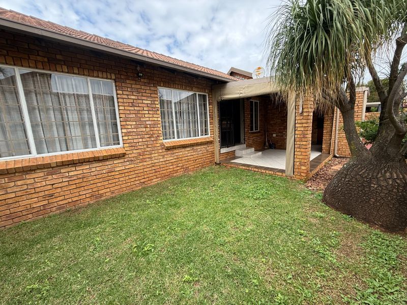 Rear view of the townhouse featuring a face brick facade, a covered patio area, and a private garden space.
