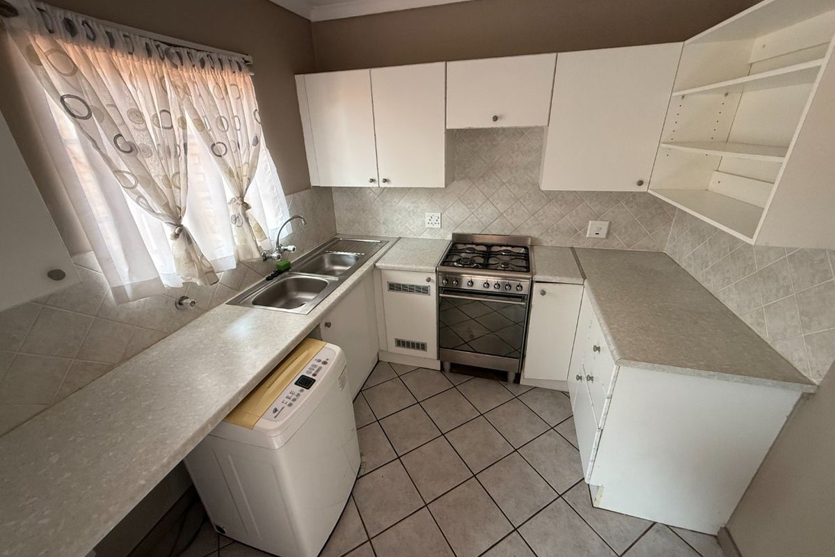 Compact kitchen featuring white cabinetry, laminate countertops, a gas stove, and tiled flooring, offering a functional layout with integrated sink and storage space.