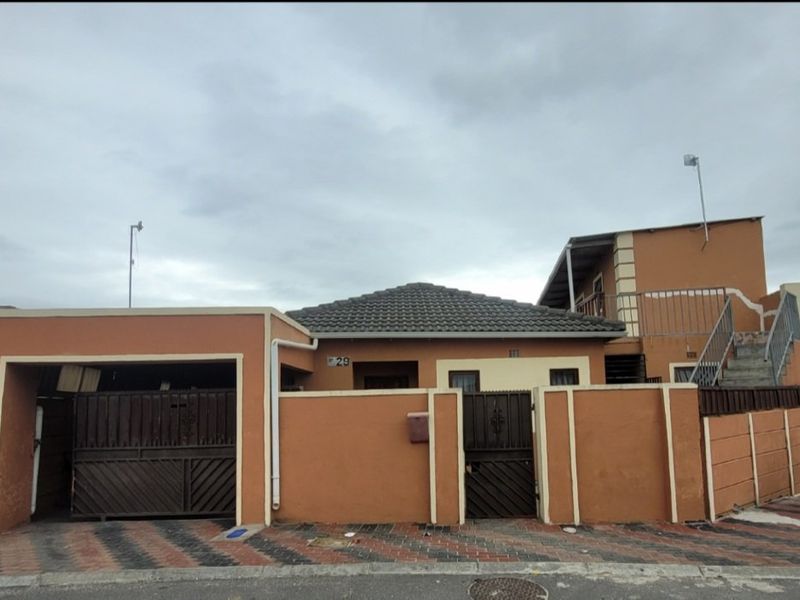 Front elevation of a residential property featuring a perimeter wall, gated driveway, and an external staircase leading to an upper level.