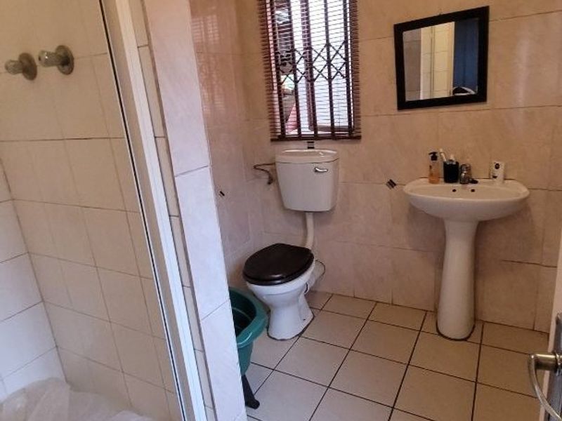 A functional bathroom featuring a shower enclosure, pedestal basin, and toilet, finished with neutral wall and floor tiles.