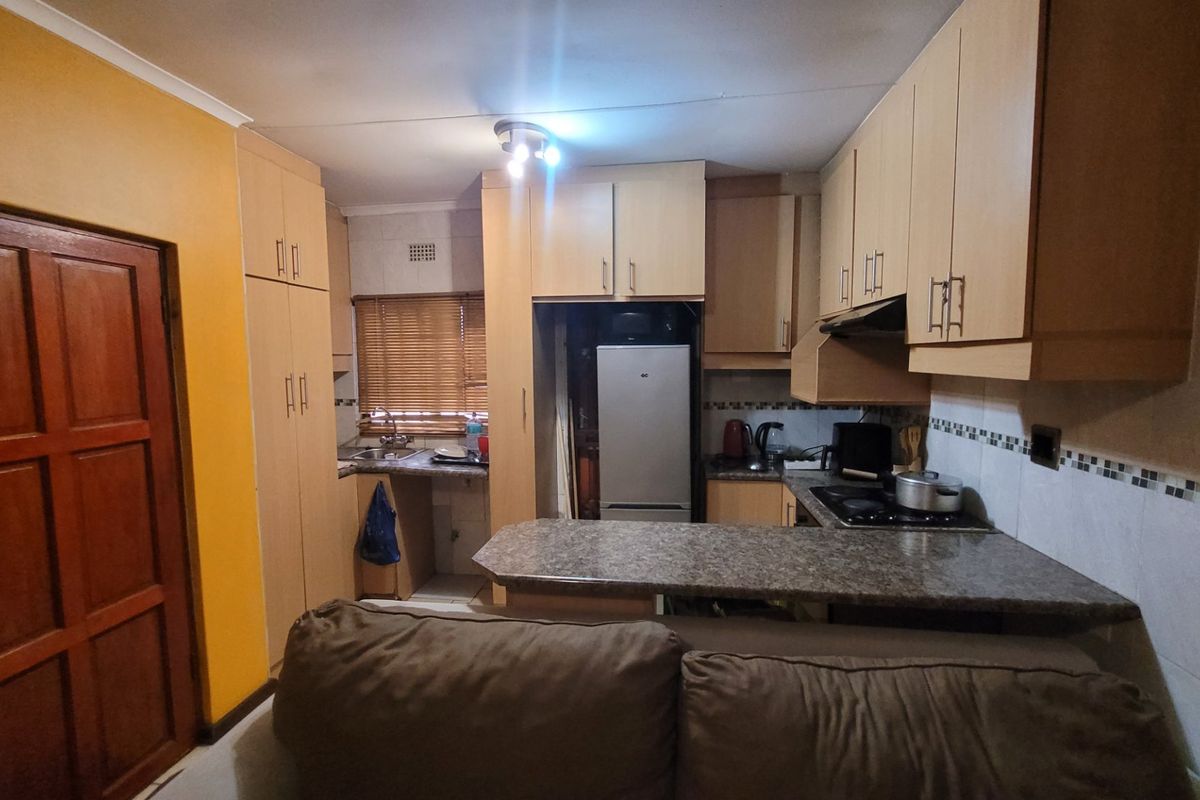 A functional kitchen featuring light wood-tone cabinetry, granite-look laminate countertops, a built-in hob with extractor fan, and a tiled backsplash.