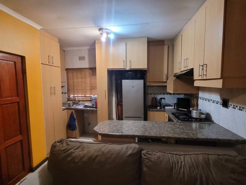 A functional kitchen featuring light wood-tone cabinetry, granite-look laminate countertops, a built-in hob with extractor fan, and a tiled backsplash.