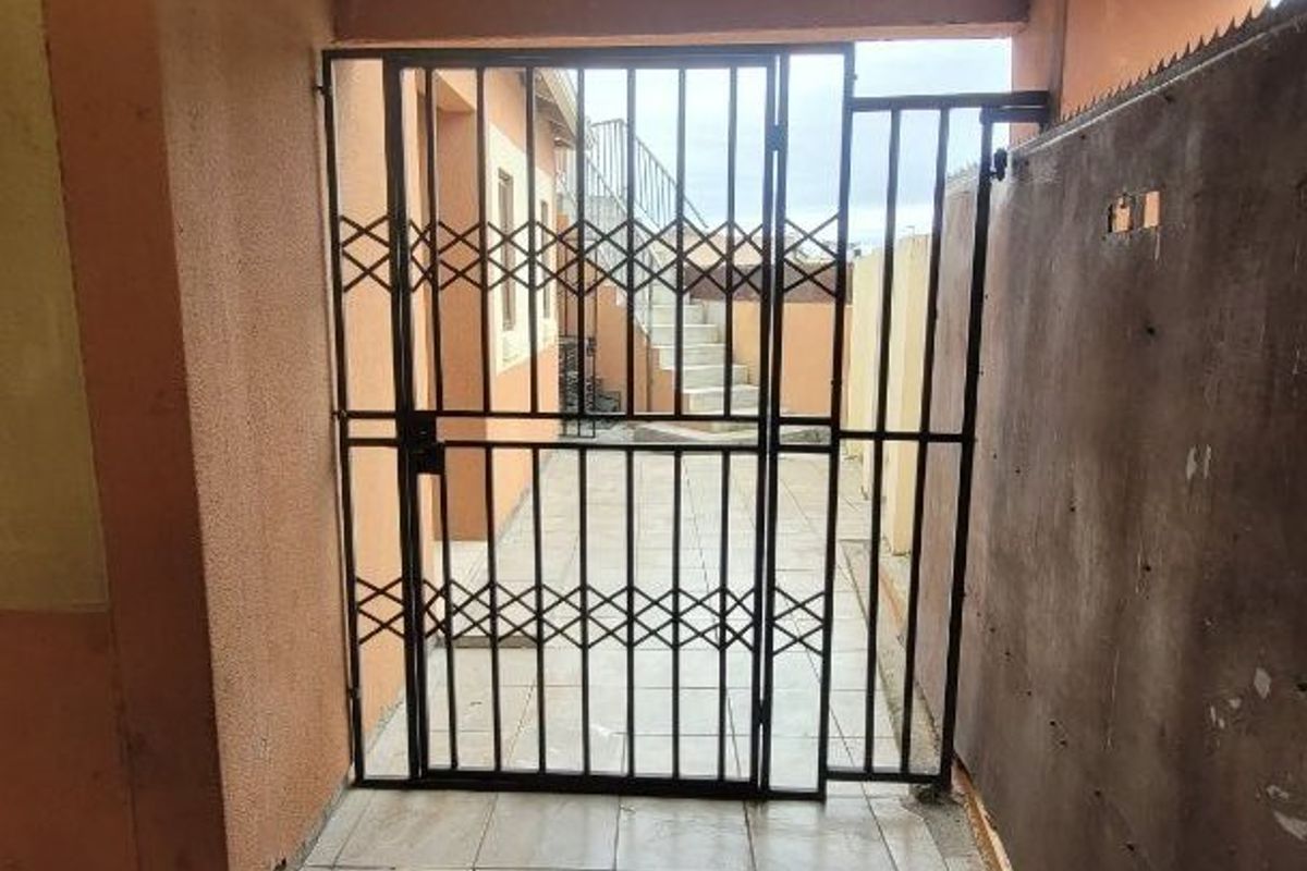 A rear exterior area featuring a security gate, paved flooring, and an external staircase under a corrugated roof structure.
