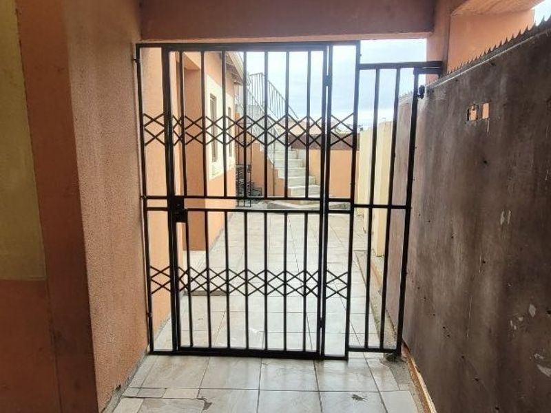 A rear exterior area featuring a security gate, paved flooring, and an external staircase under a corrugated roof structure.