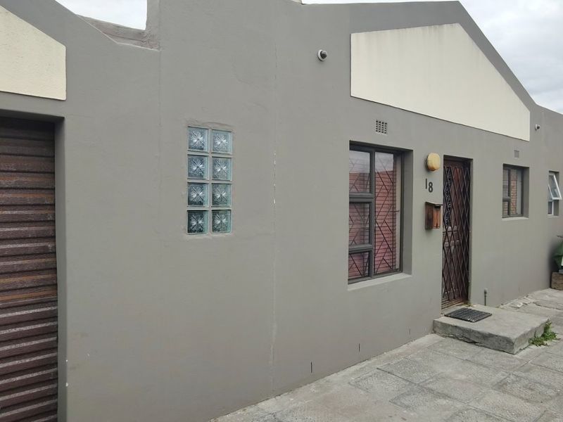 Front elevation of the property featuring a roller shutter garage door, security gate, and paved entrance area.