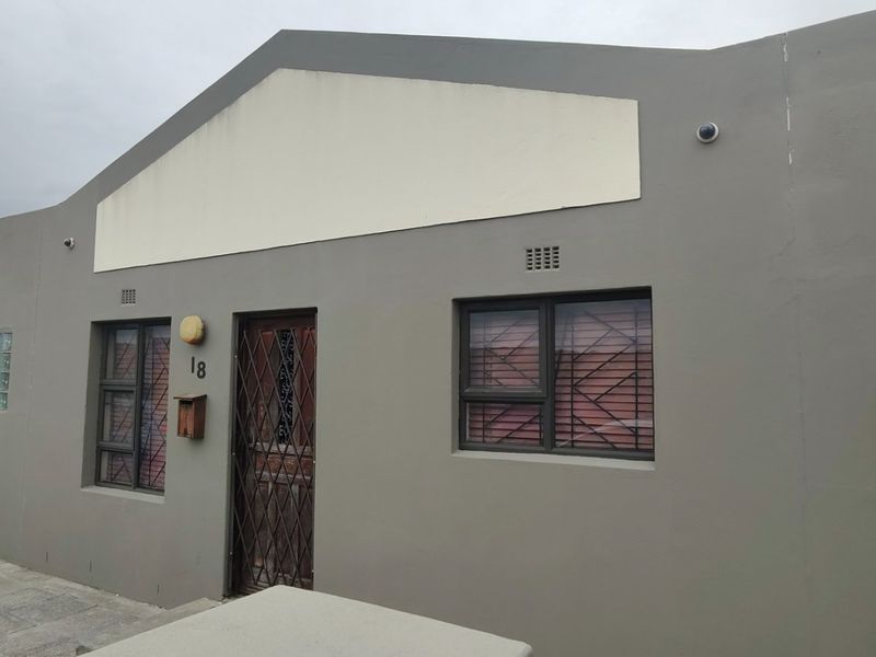 Front elevation of a residential property featuring a grey rendered facade, security gates, and a single garage.