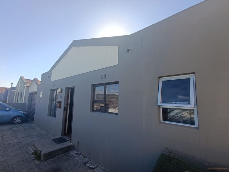 Front elevation of a residential property featuring grey painted exterior walls, aluminium window frames, and a paved entrance area.