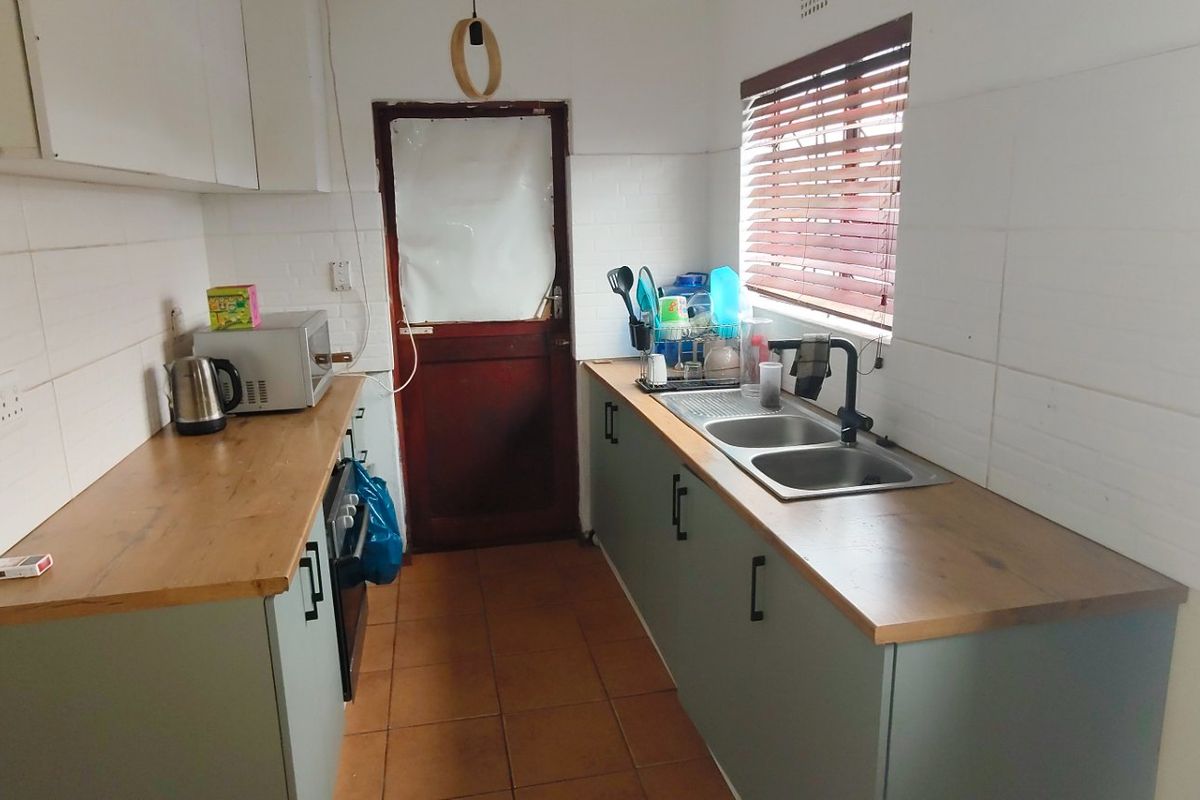 A functional galley-style kitchen featuring modern laminate countertops, double sink, tiled splashbacks, and ample built-in cabinetry with a direct exterior access door.