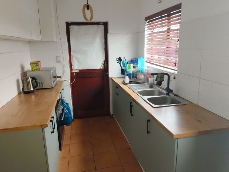 A functional galley-style kitchen featuring modern laminate countertops, double sink, tiled splashbacks, and ample built-in cabinetry with a direct exterior access door.