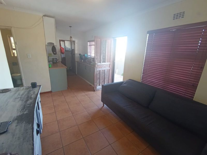 Open plan living and kitchen area featuring tiled flooring, timber door access, and venetian blinds, offering a functional layout with potential for cosmetic updates.