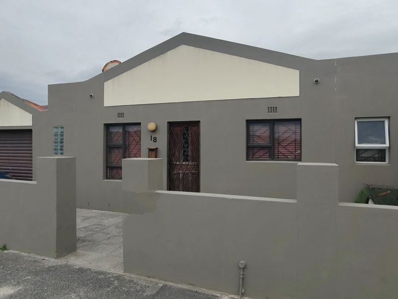 Front elevation of a single-story house featuring a paved driveway, boundary wall, and secure entrance with security gate and bars.