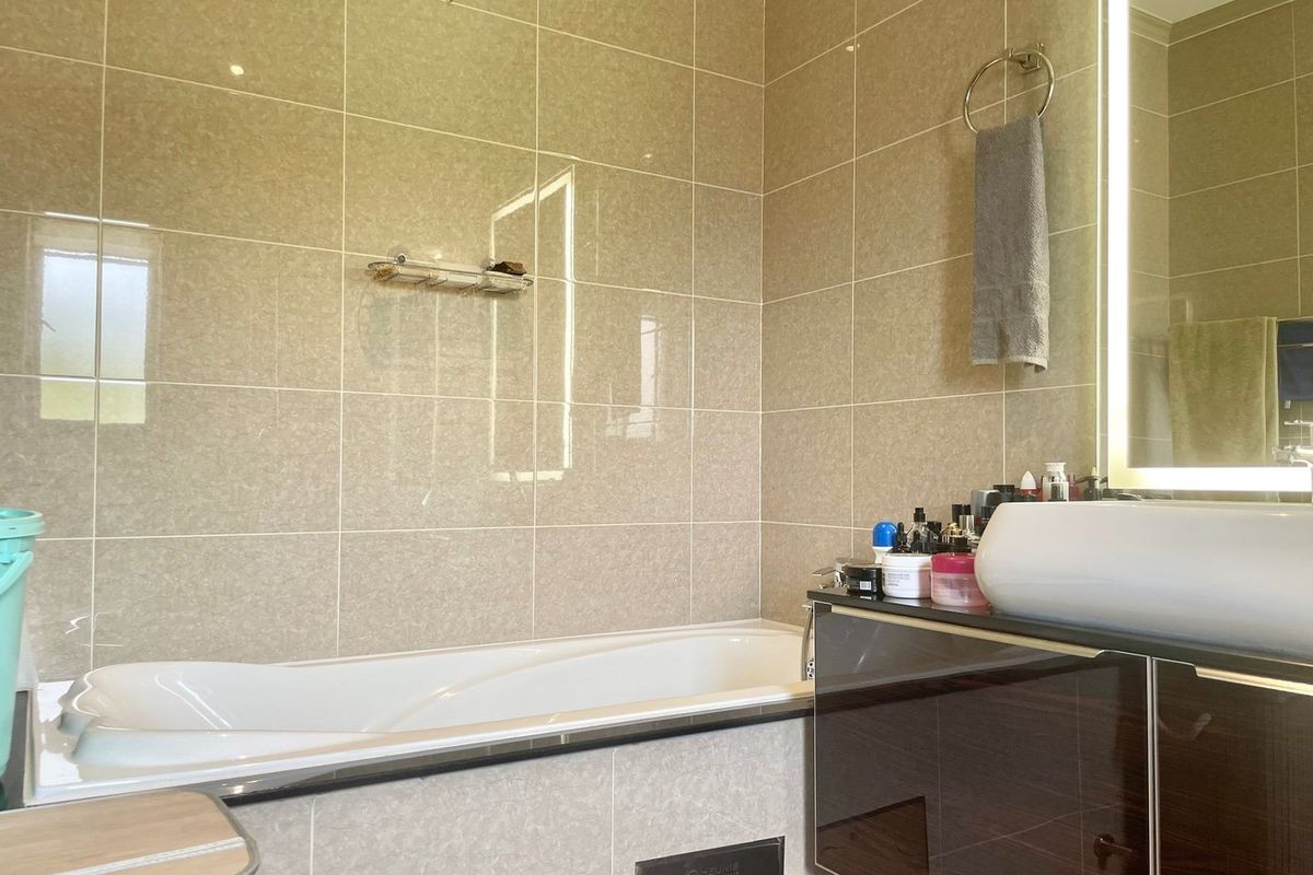 A modern bathroom featuring a built-in bathtub, tiled walls, and a vanity unit with an integrated basin and illuminated mirror.