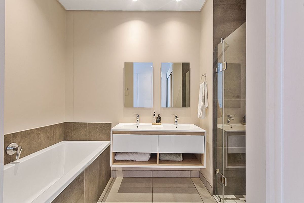 Modern bathroom featuring a double vanity, built-in bathtub, and a separate glass-enclosed shower with neutral tile finishes.