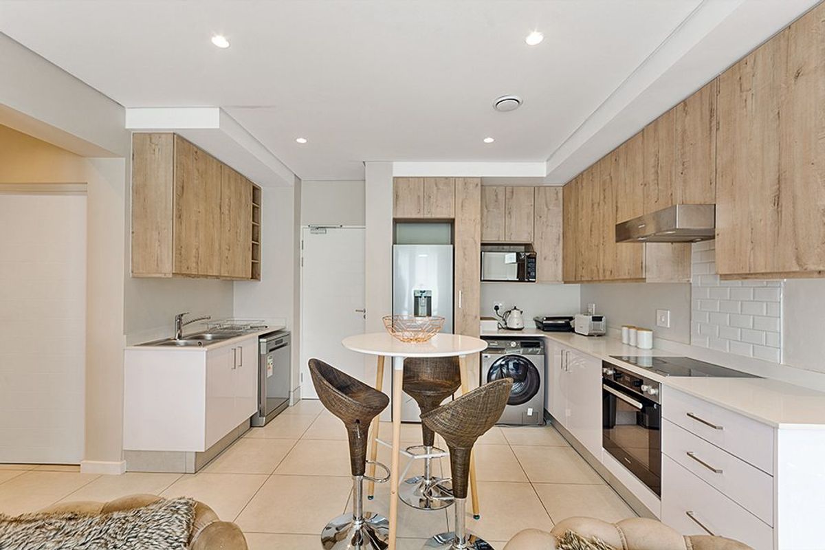 Modern kitchen featuring light wood-grain cabinetry, stone countertops, subway tile backsplash, and integrated stainless steel appliances, including an oven and hob.