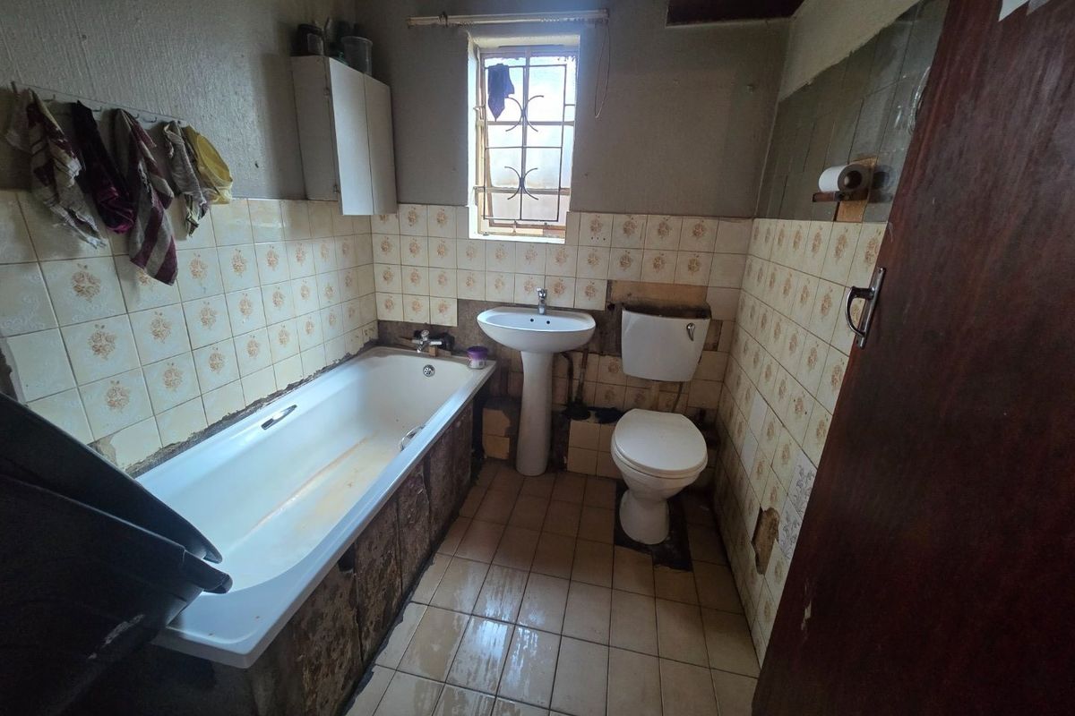 A dated bathroom featuring a bathtub, pedestal basin, and toilet, requiring significant renovation and cosmetic updates to improve its condition and functionality.